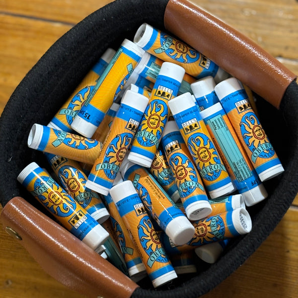 Lip balm tube with light blue background and Oberon Ale logo. Has a Tamper seal.