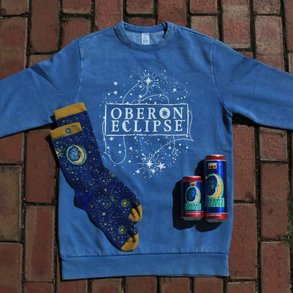Blue sweatshirt with 'Oberon Eclipse' branding on a brick surface, with deep blue star patterned socks with Oberon Eclipse branding