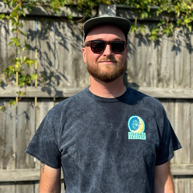 Short Sleeve Tee, Navy Acid Wash, with large logo on the back "Oberon Eclipse" at the top, Oberon Eclipse logo in the center and "Its Polite toe Stare: at the bottom. Oberon eclipse logo on the right chest pocket.