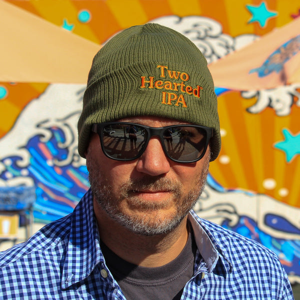 Man wearing a green 'Two Hearted IPA' beanie with orange embroidered text logo with green outline