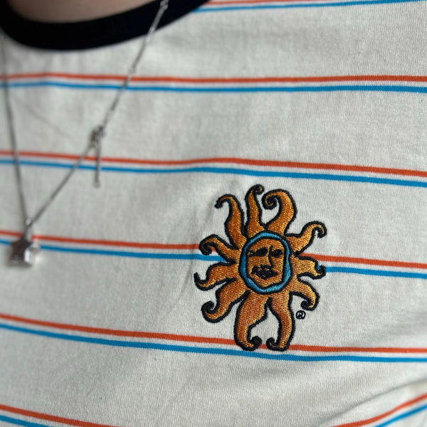 off white tee with orange and blue stripes with a black collar, featuring a full color embroidered Oberon sun on the left pocket.  