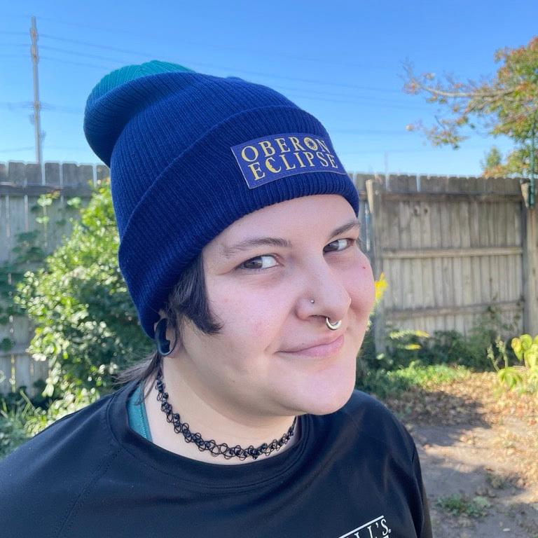 beanie hat with light blue fading to deep blue via gradient dye.  Also features patch at front with Oberon Eclipse lettered in yellow against deep blue back