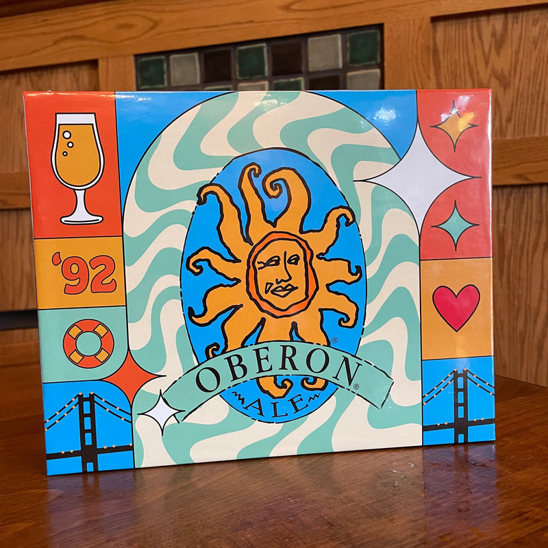 1000 piece puzzle featuring a design that incorporates the Oberon brand logo and beer glasses, hearts, the year 1992, waves, all in the color palette used for Oberon.  Orange, gold, blue and sea foam green