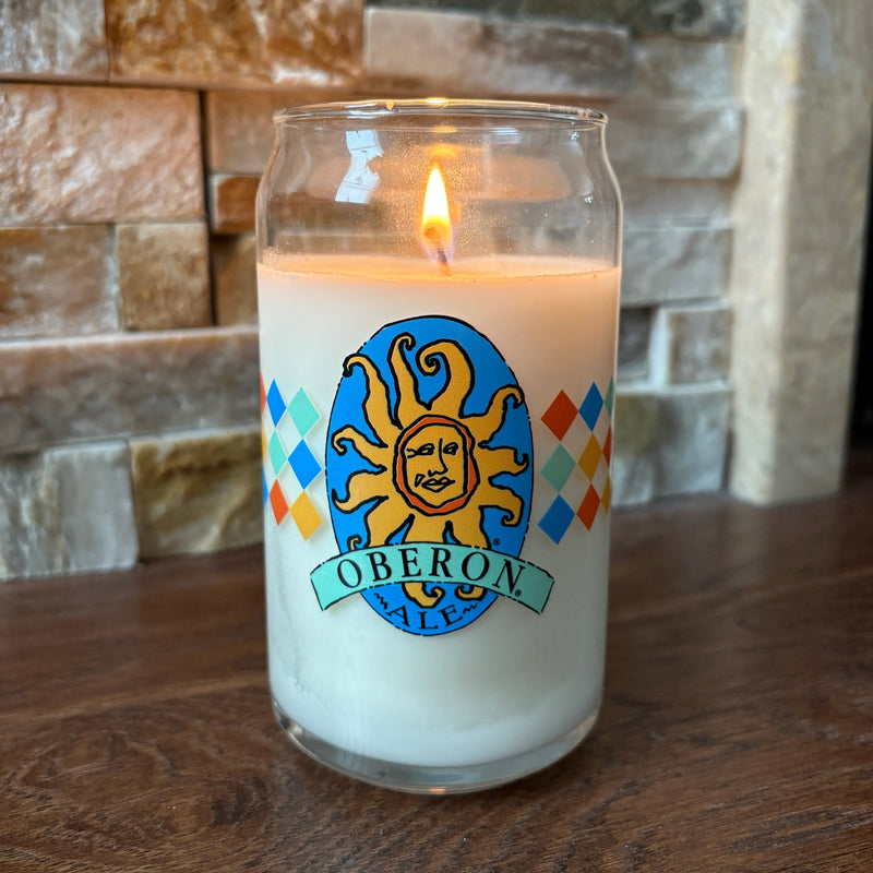 Can glass white candle with full color Oberon logo on front and 3 stripes of multicolored diamonds in orange, teal, blue, and gold