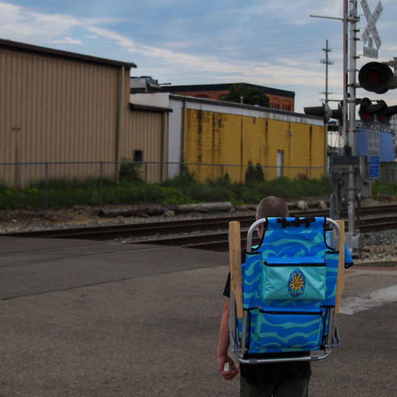 Person with a blue backpack walking near train tracks and buildings.