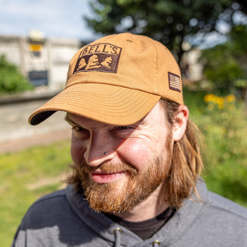 Tan twill baseball cap with black embroidered Bell's logo on the front and an American flag embroidered on the side.