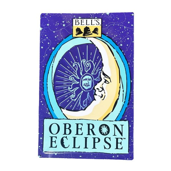 Rectangular tin sign featuring Oberon Eclipse art, including light blue stars, constellations, and dotted lines on a dark blue background. Bell's logo in black, white, and yellow is top center. Oberon Eclipse moon in varying shades of blue and yellow with Oberon outline inside. Oberon Eclipse in black on a light blue background at the bottom.