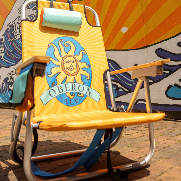 beach chair with light orange and dark orange sunburst from center. Center back features Oberon Ale logo. Teal head rest pillow  at the top of the chair. 