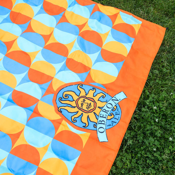 Orange framed circular patterns with alternating colors, light and dark blues as well as gold and orange.  Underside is full blue.  Oberon logo large center placement at the bottom of blanket.