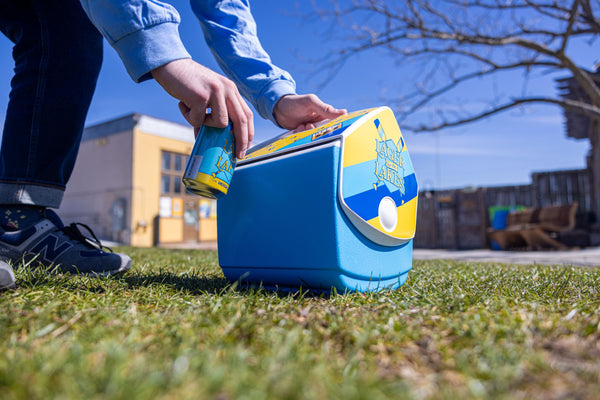 Light blue Igloo cooler with yellow and blue striping on the side panel with Lager for the Lakes Logo. Top of tent style lid has yellow backfground with blue paddles and a Bell's logo.