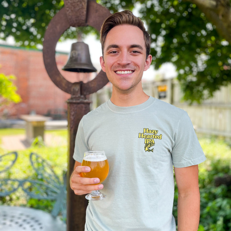 light dusty green short sleeve tee with Hazy Hearted IPA logo and trout in yellow font with dark green outline on pocket area in front