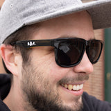 Black malibu style sunglasses with white Bells logo on stems.  Inside of stems are yellow