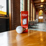 Three white golf balls. The leftmost ball features the Bell's Logo with "Inspired Brewing " tagline. The middle golf ball has the Titleist logo in black and a red 4. The right glf ball says DT TruSoft in black lettering
