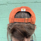 Person wearing a rust orange corduroy cap, back view of buckle strap and Oberon sun pinch tag