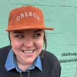 Person wearing a rust orange corduroy cap with white 'Oberon' text 