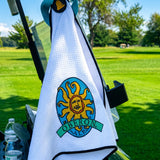 black bordered white waffle knit golf towel with blue handle and large full color Oberon sun logo embroidered. also features circular black magnet with yellow bell logo