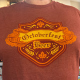  a heathered rust-red t-shirt with a large orange and yellow graphic on the chest that reads 'Octoberfest Beer' inside an ornate crest design.