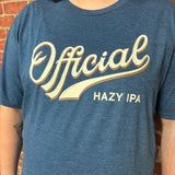 A person wearing a heathered blue graphic T-shirt with large cream lettering that reads 'Official' and smaller text 'HAZY IPA' on the front