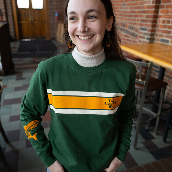 dark green long sleeve tee shirt with single orange stripe in the chest area and one cream stripe above and below.  Two Hearted IPA logo in dark green on the left pocket, and orange trout logo on the forearm area of right sleeve