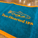 Deep green towel with orange borders, orange “Two Hearted IPA” text and orange fish logo above it