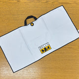black bordered white waffle knit golf towel with blue handle and large full color Bell's logo embroidered. also features circular black magnet with yellow bell logo