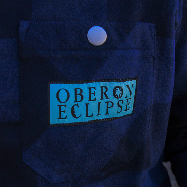blue plaid flannel shacket with light blue embroidered patch with Oberon Eclipse text logo on pocket.  