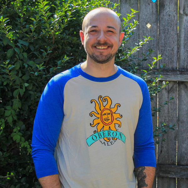 oat colored baseball tee with blue sleeves and neck.  full color Oberon logo on front