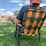 Person sitting on a green and orange checkered folding lawn chair 