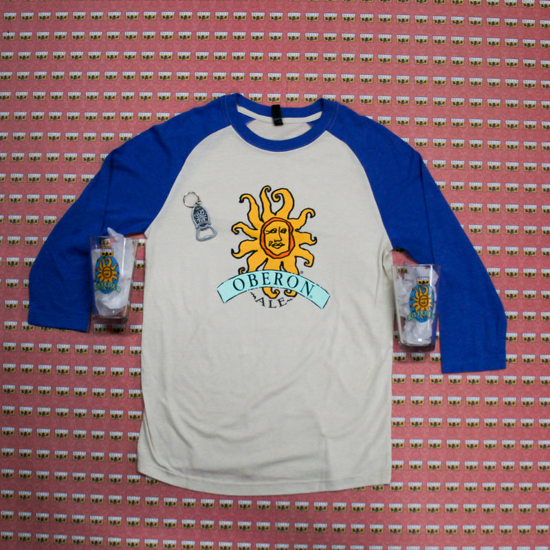 Oberon baseball tee, blue sleeves with large Oberon logo on the front. 2 Obeorn pint glasses and a silver oberon logo bottle opener keychain. 