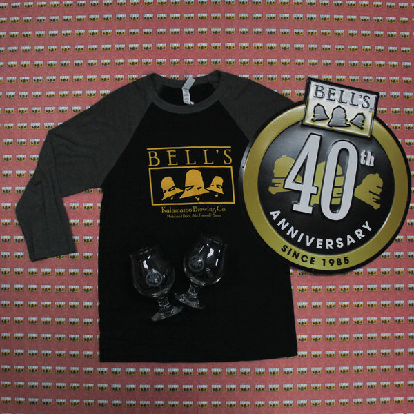 black and gray raglan tee with vintage yellow bell's logo, 40th anniversary tin tacker with gold circle and gold bells inside, full color logo on top, and since 1985 at bottom inside circle.  40th Anniversary in white over the Bells in sign.  There are also two snifter glasses vwith 40th Anniversary logo etched in.