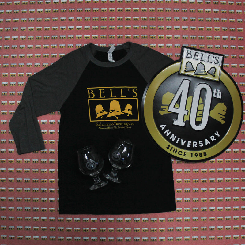 black and gray raglan tee with vintage yellow bell's logo, 40th anniversary tin tacker with gold circle and gold bells inside, full color logo on top, and since 1985 at bottom inside circle.  40th Anniversary in white over the Bells in sign.  There are also two snifter glasses vwith 40th Anniversary logo etched in.